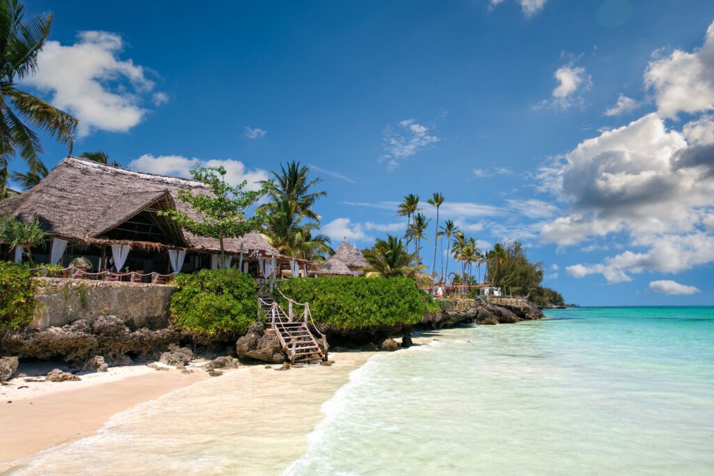 Idyllic beachfront scene in Zanzibar with palm trees, turquoise sea, and a traditional villa.